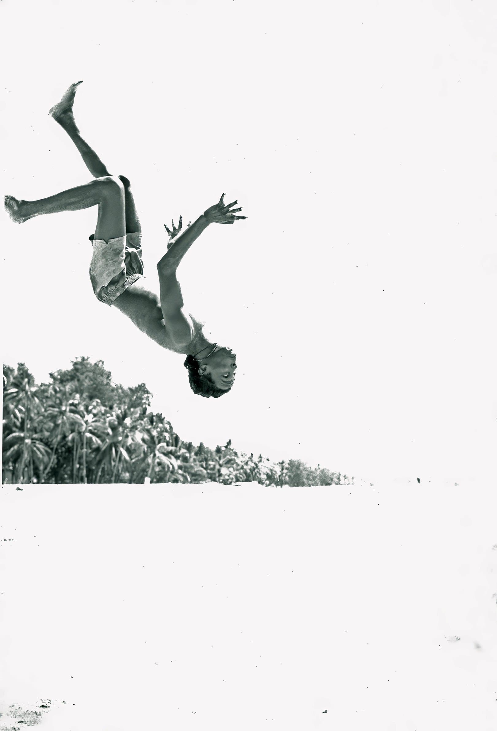 An acrobat flipping above palm trees