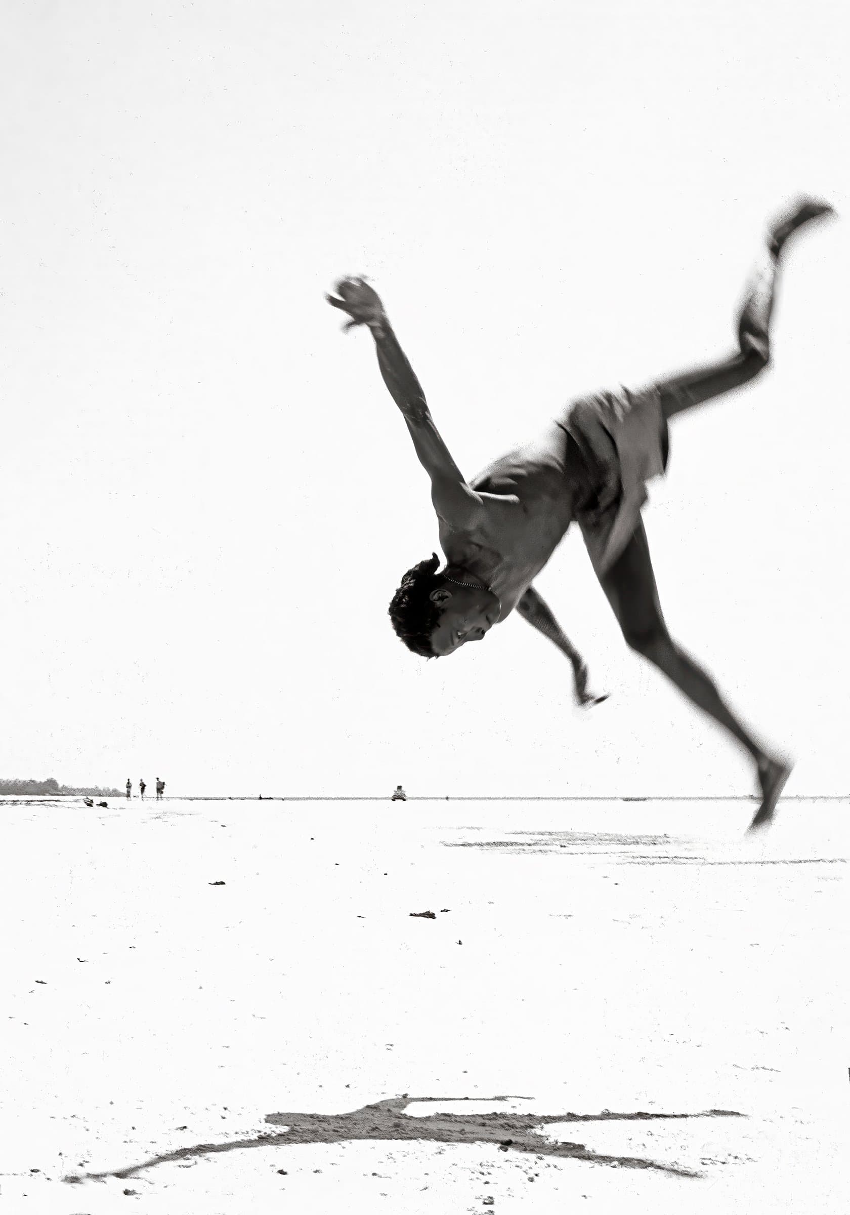 An acrobat mid-flip above a white beach